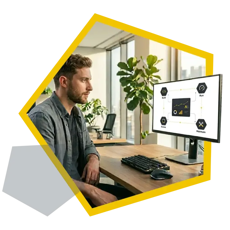 Eine Person sitzt an einem Arbeitsplatz und betrachtet auf einem Monitor ein Diagramm zum Anwendungsmanagement, das die Bereiche „Build“, „Run“, „Maintain“ und „Evolve“ zeigt.