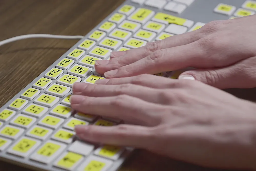 Zwei Hände auf einer Tastatur mit Tasten-Beschriftung für seheingeschränkte Menschen
