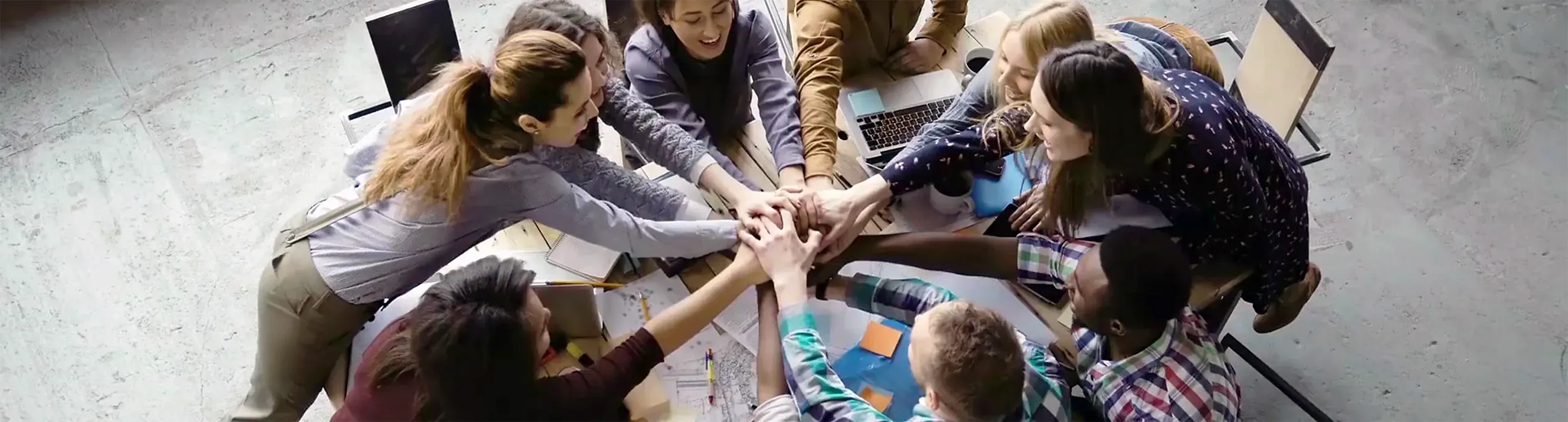 Teamwork bei der AM GmbH mit mehreren Mitarbeitenden an einem Tisch, die ihre Hände übereinander halten